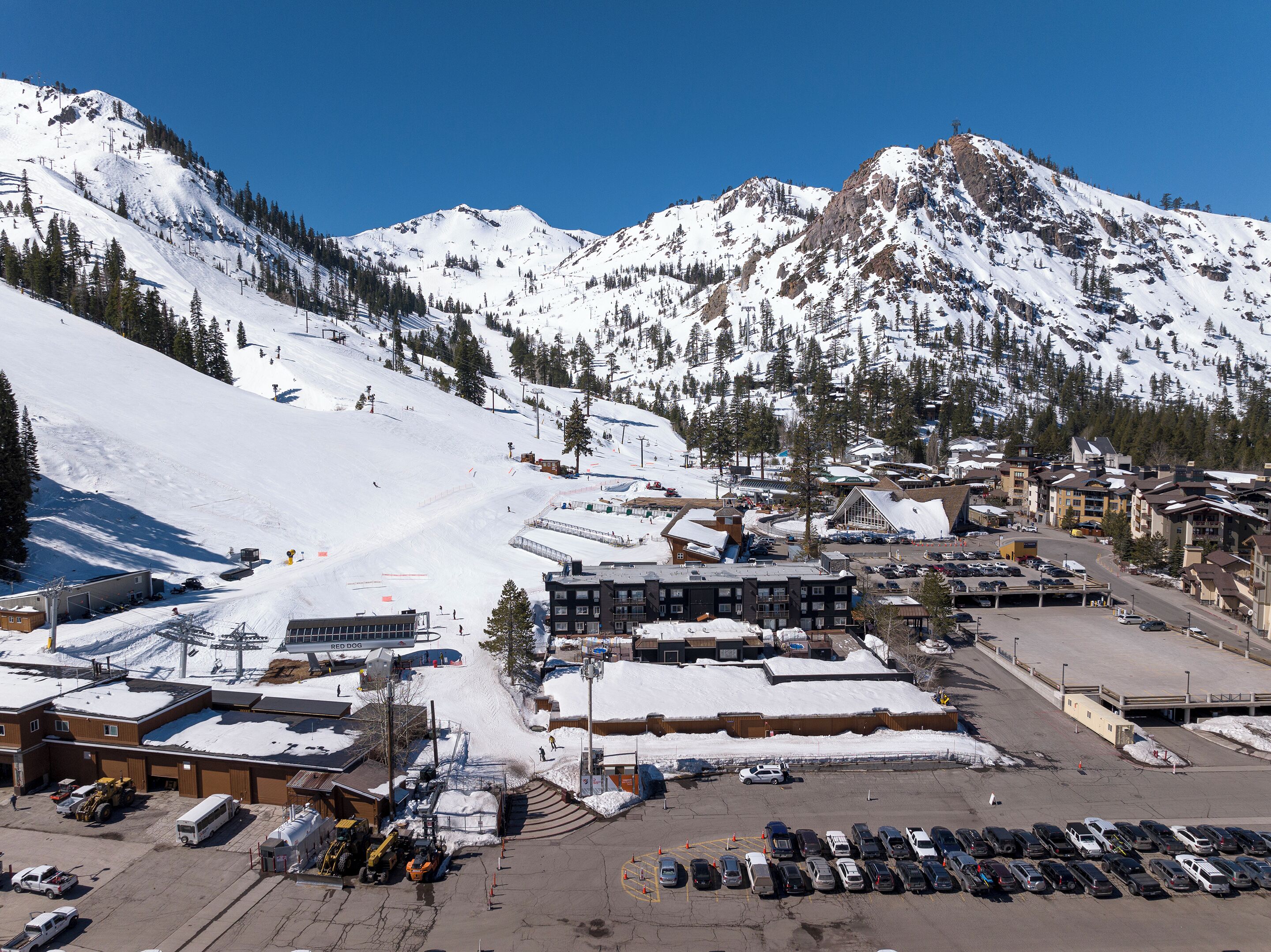 A ski resort with a parking lot, buildings, and a mountain backdrop.