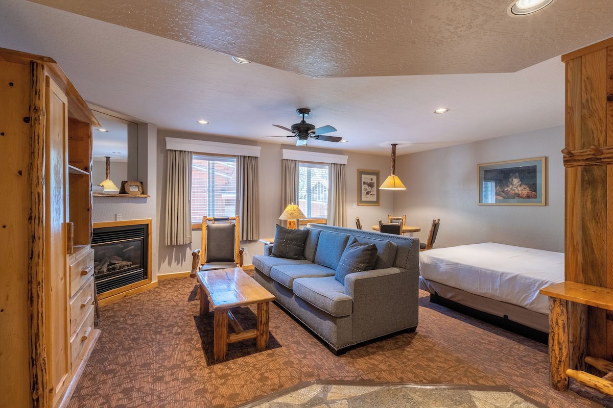 A cozy room with a sofa, a bed, a wooden cabinet, a fireplace, and a ceiling fan.