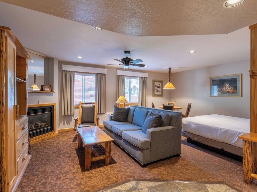 A cozy room with a sofa, a bed, a wooden cabinet, a fireplace, and a ceiling fan.
