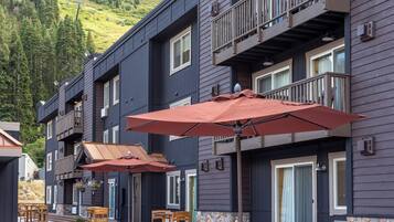 A multi-story building with balconies, outdoor seating with umbrellas, and a stone wall.