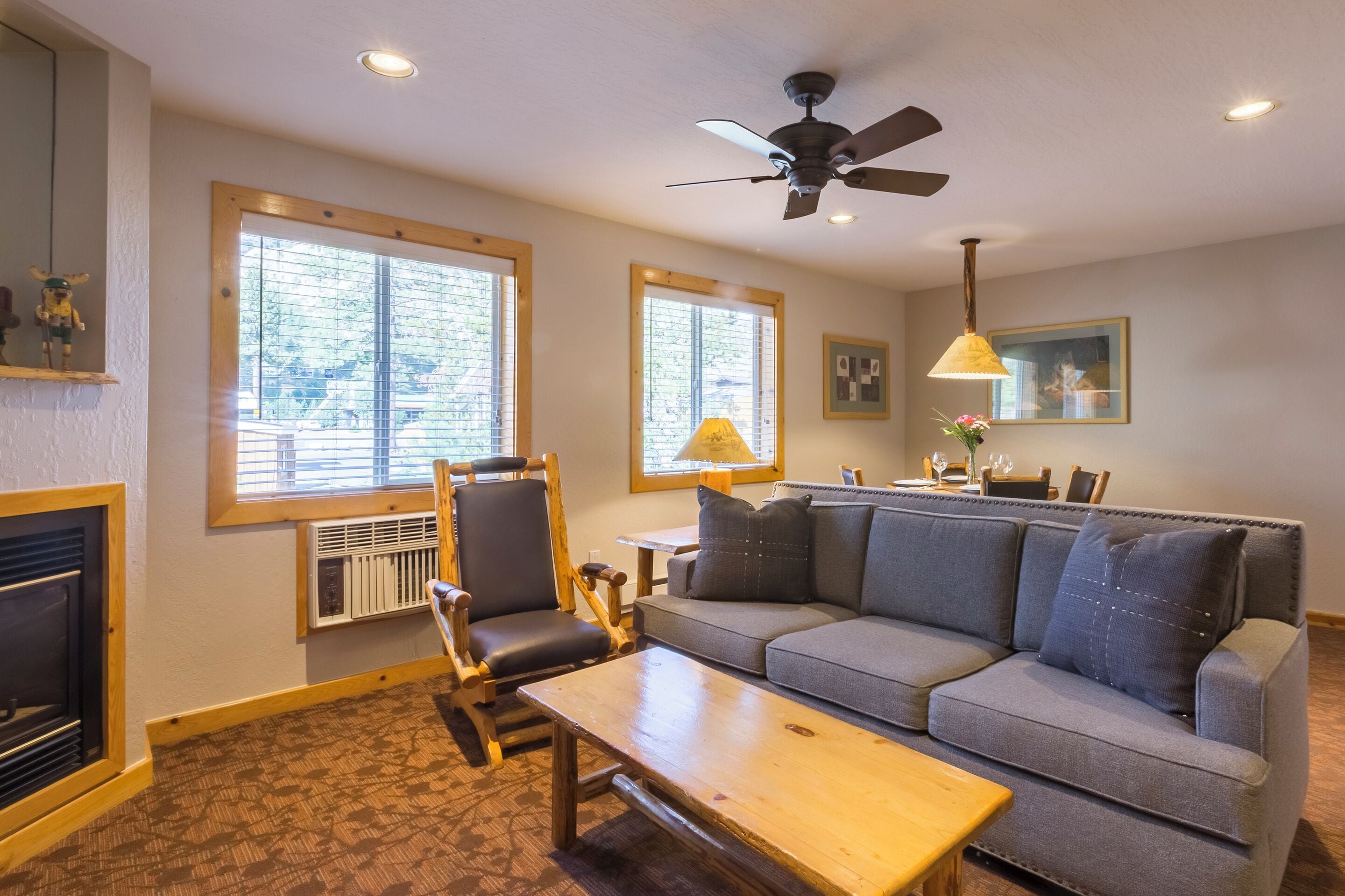 A cozy living room with a fireplace, a sofa, a wooden table, and a ceiling fan.
