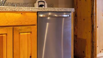 Lavastoviglie in acciaio inossidabile integrata sotto un piano di lavoro in granito, in una cucina con mobili in legno.