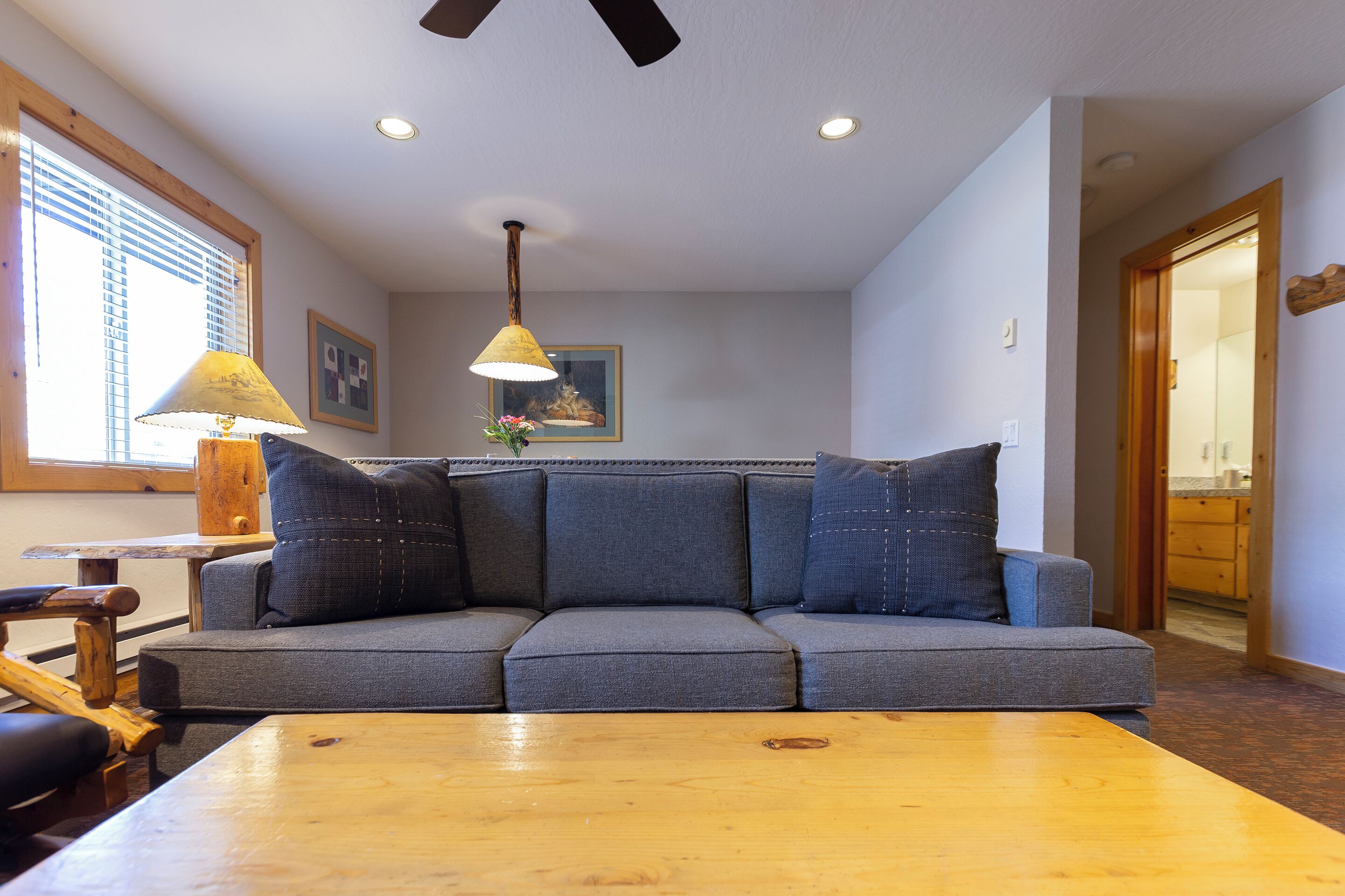 A living room with a gray sectional sofa, wooden coffee table, and a ceiling fan.