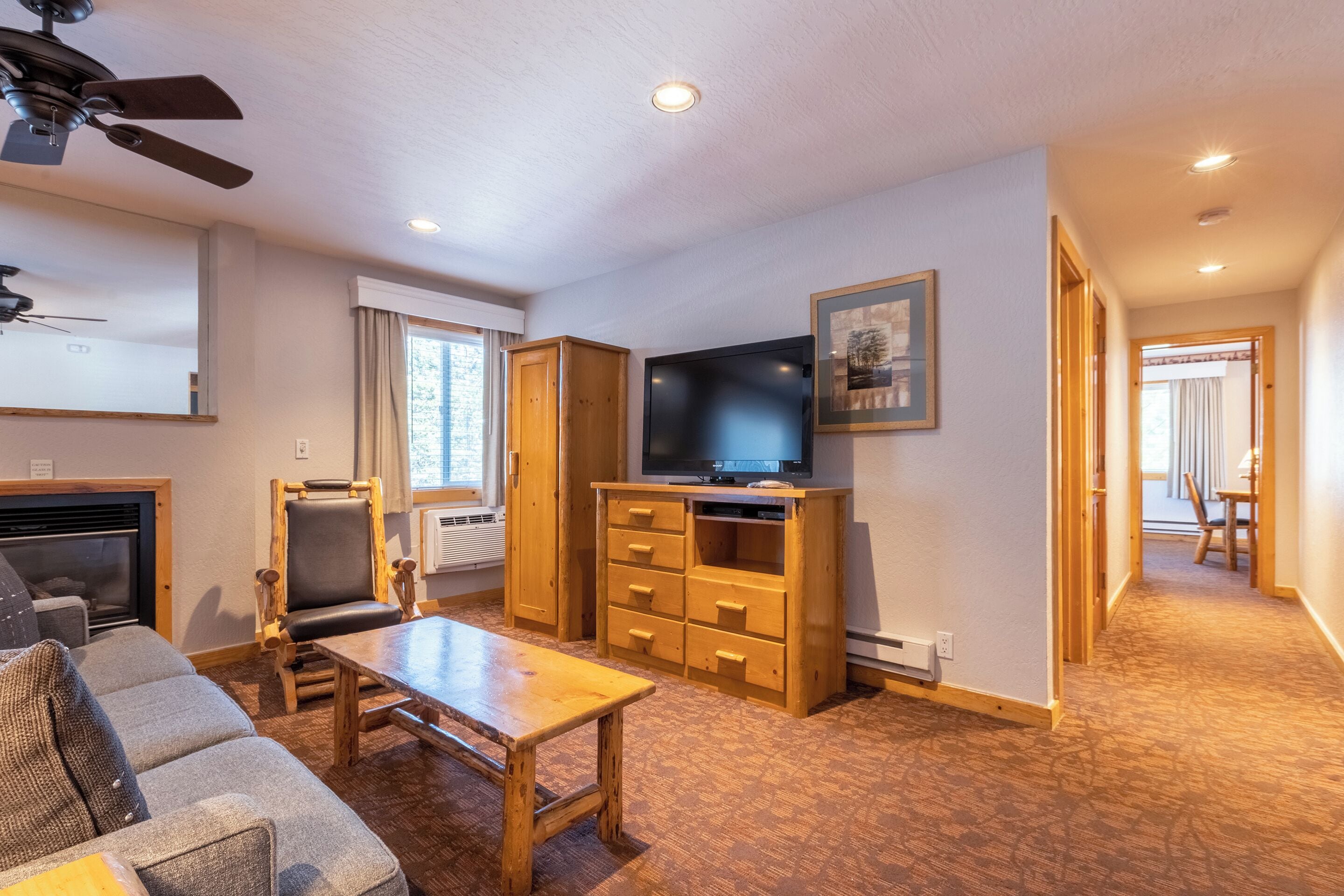 A living room with a fireplace, a television, a wooden cabinet, and a ceiling fan.
