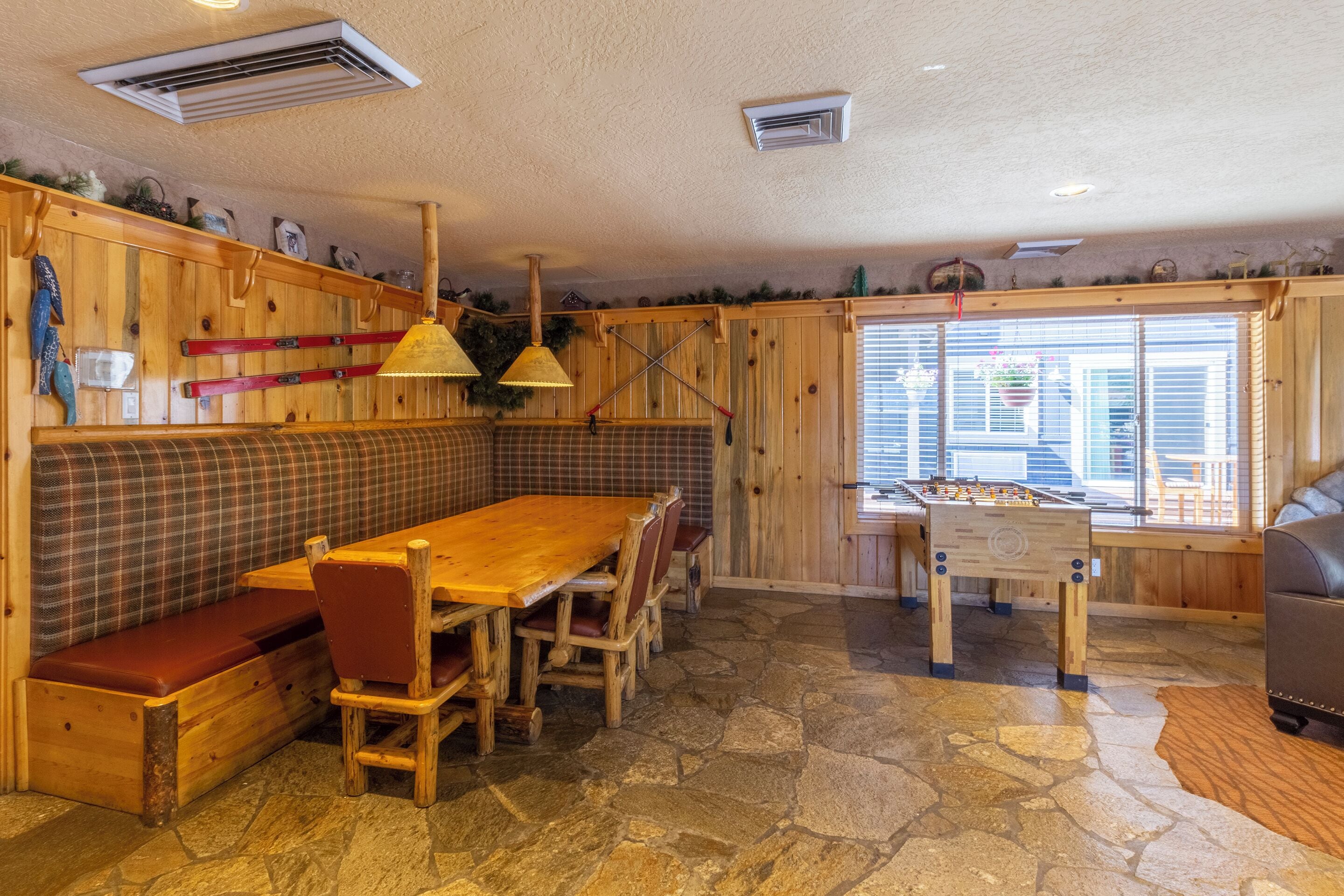 Un interior acogedor de madera con piso de piedra, una mesa de madera con sillas, un banco y una mesa de futbolín.