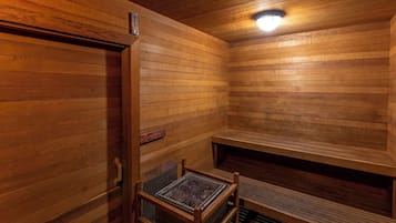 A wooden sauna with a bench, a door, and a light fixture.