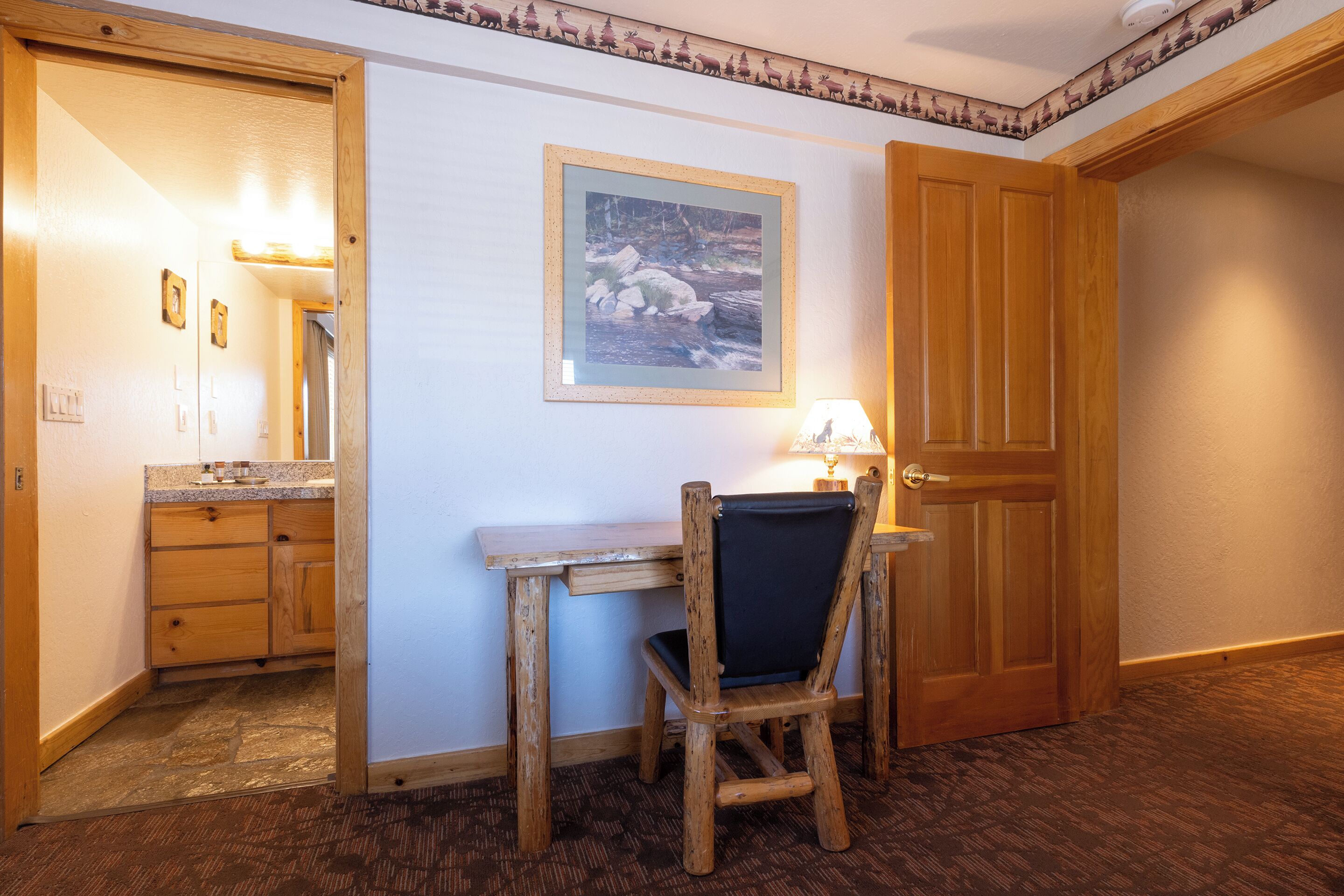 A wooden desk with a chair, a framed picture on the wall, and a wooden door.