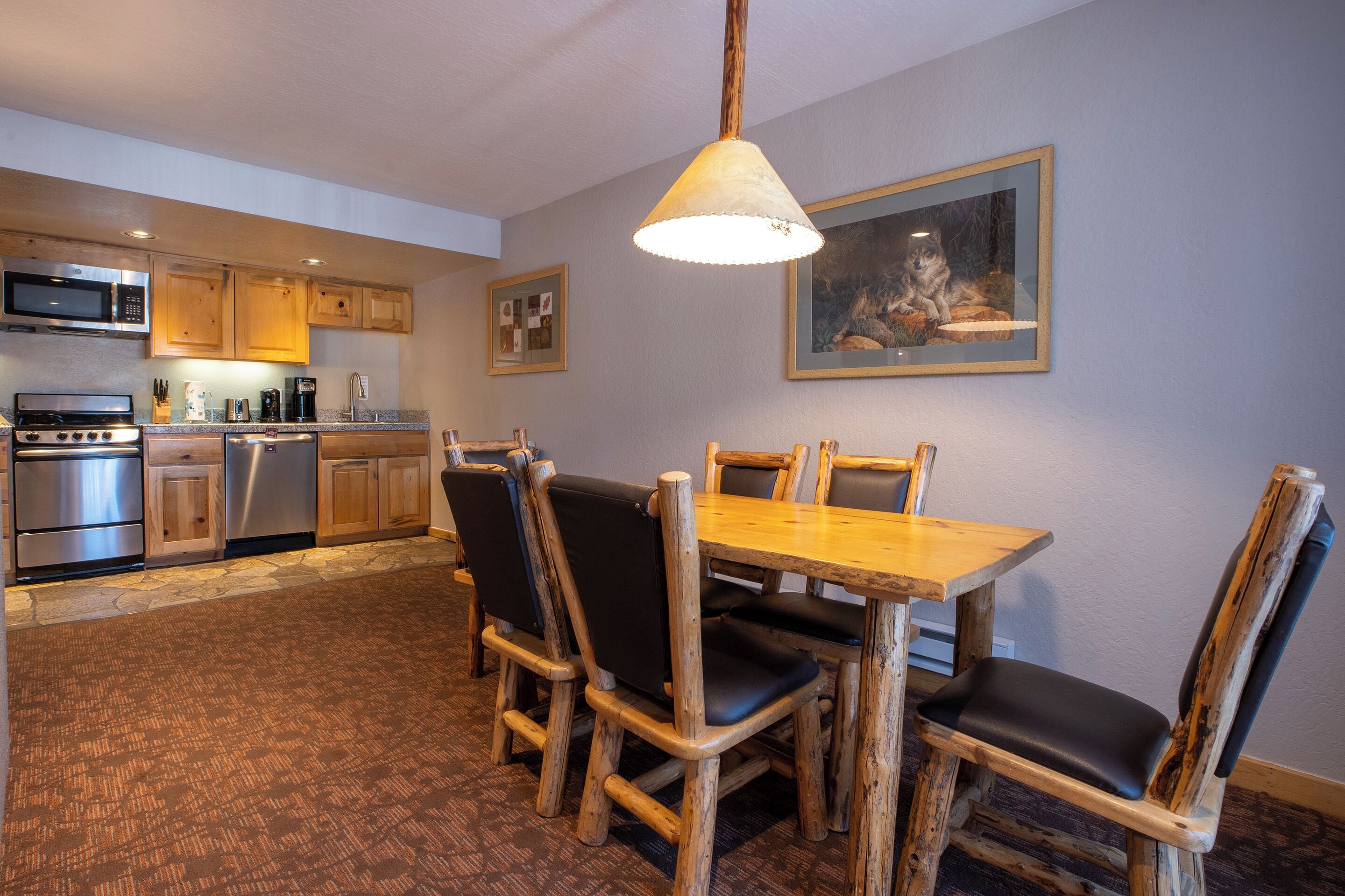 Une cuisine avec des meubles de rangement en bois, une table à manger avec des chaises et un luminaire suspendu.
