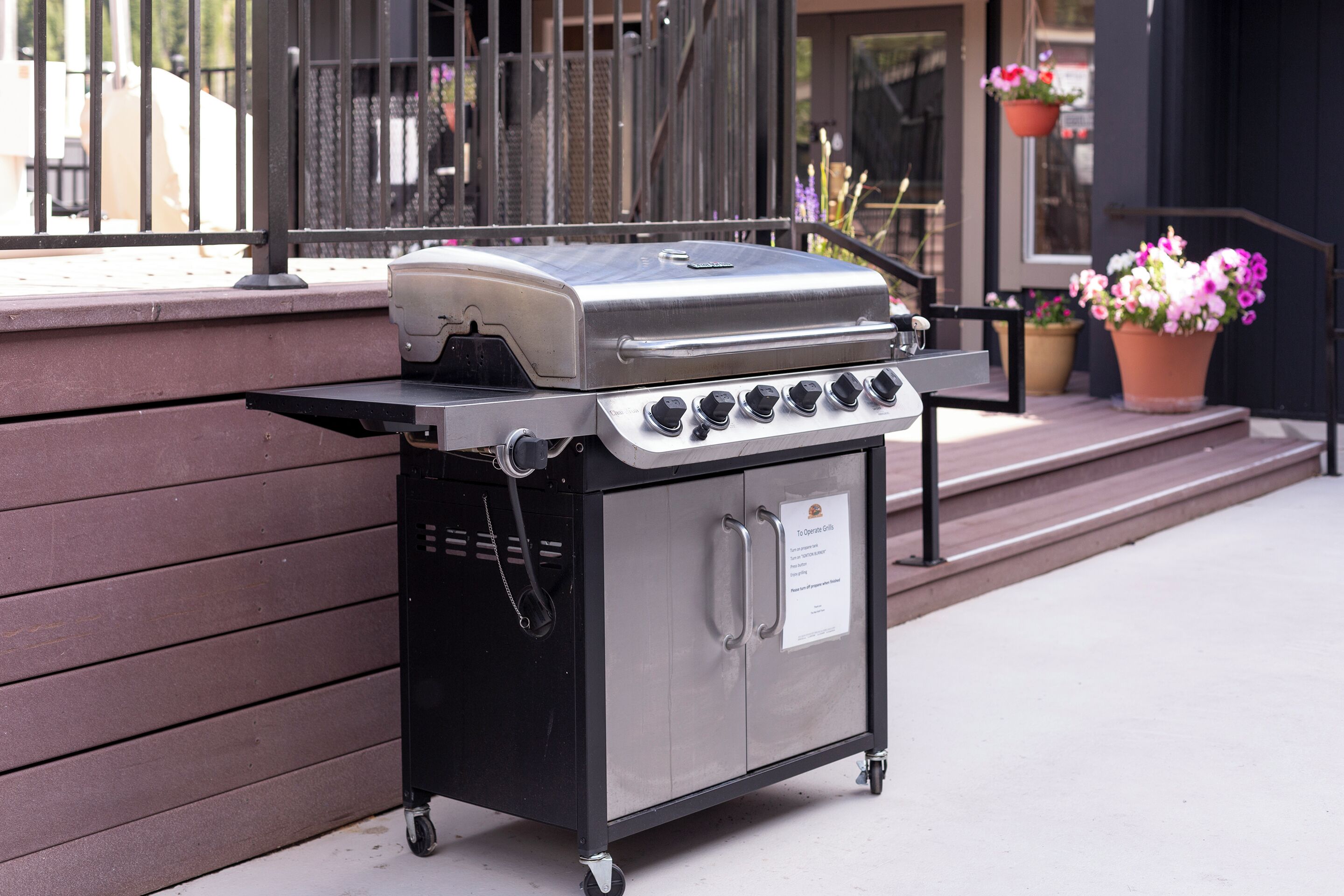 A portable stainless steel grill with a control panel and a storage compartment, placed on a wheeled cart.