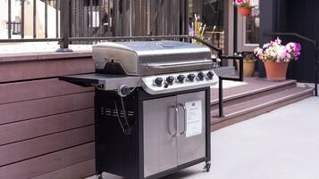 A portable stainless steel grill with a control panel and a storage compartment, placed on a wheeled cart.