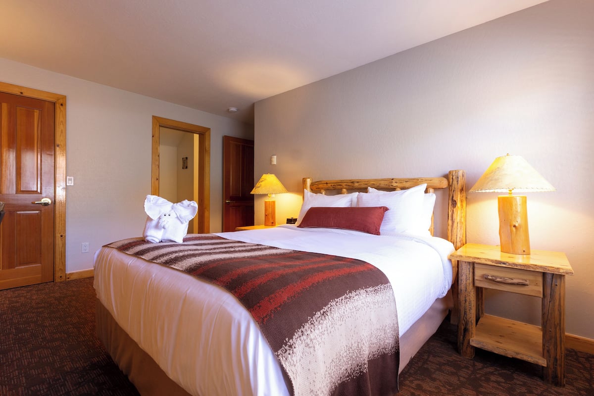 A hotel room with a large bed, wooden headboard, two bedside lamps, and a wooden nightstand.