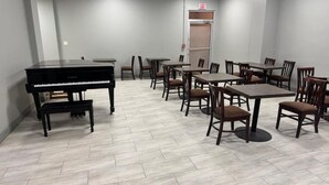 Una habitación con piano, mesas y sillas dispuestas para una reunión o evento.