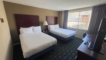 A hotel room with two beds, a desk with a TV, and a window with a city view.