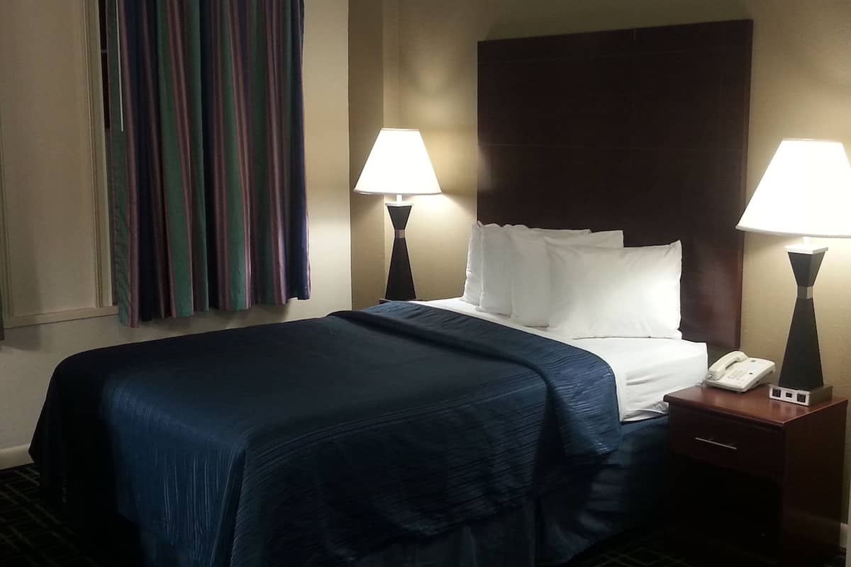 A hotel room with a bed, two bedside lamps, a telephone, and a striped curtain.