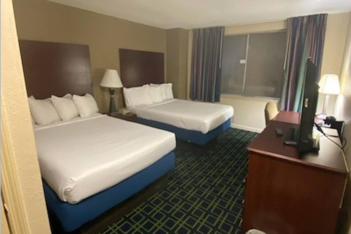 A hotel room with two beds, a desk, a chair, and a window with curtains.