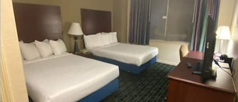 A hotel room with two beds, a desk, a chair, and a window with curtains.