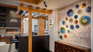 A modern interior with a stone fireplace, wooden beams, and a wall of colorful glass art.
