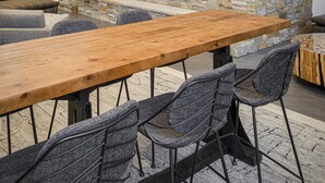 A modern outdoor dining area with a stone fireplace, wooden table, and metal chairs.