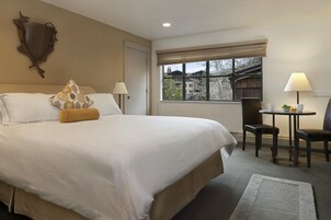 Habitación de hotel con una cama grande, dos lámparas de noche, una mesita con sillas y vistas al exterior a través de una ventana.