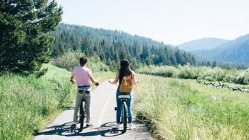 Deux personnes à vélo sur une route de campagne, avec une montagne boisée en arrière-plan.