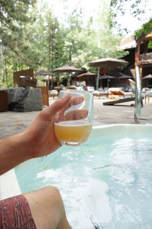 A person holding a glass of beer near a pool with lounge chairs and umbrellas in the background. - PlumpJack Inn (Olympic Valley)
