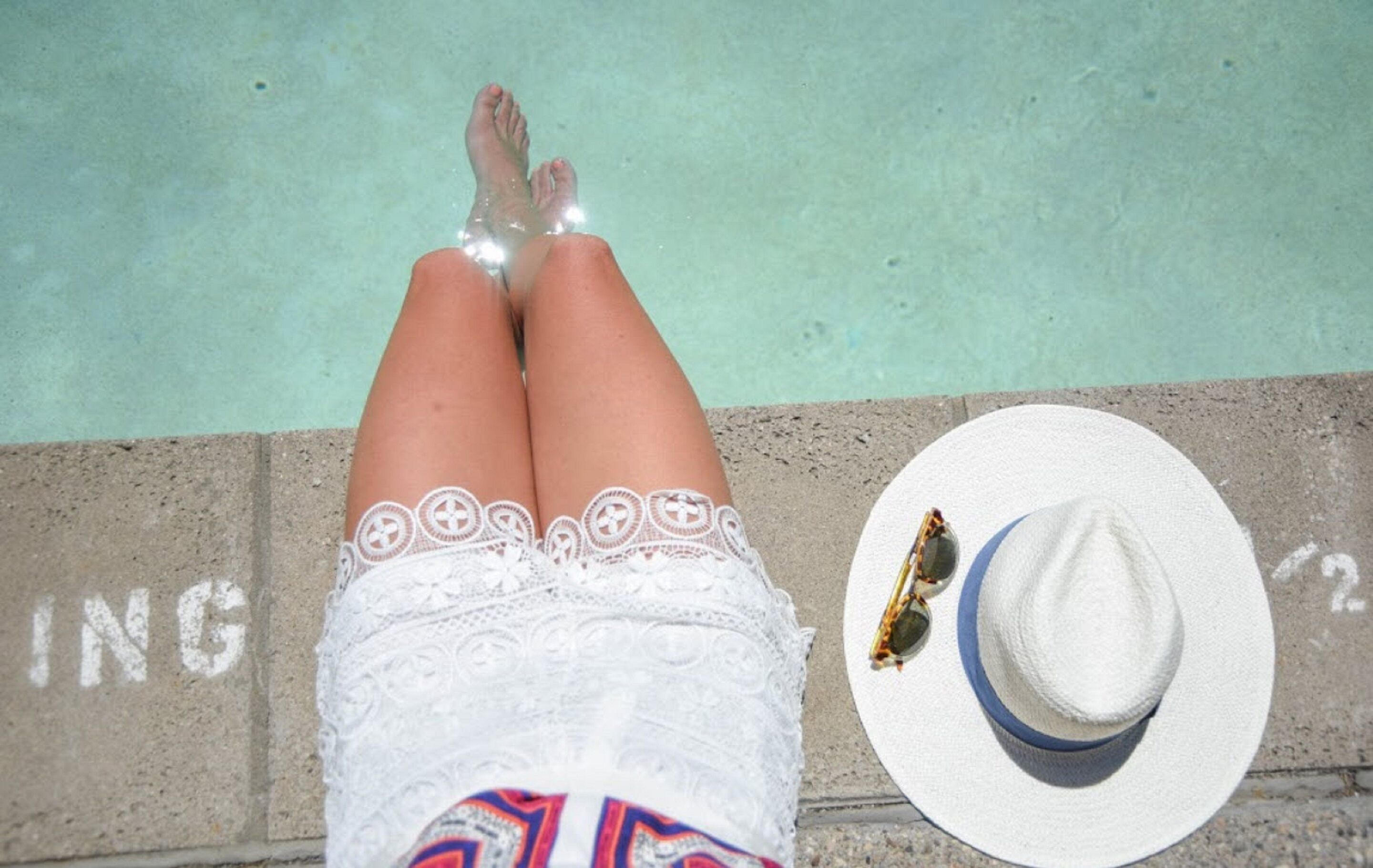 Eine Person liegt am Pool, neben ihr ein weißer Hut und eine Sonnenbrille.