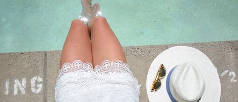 Eine Person liegt am Pool, neben ihr ein weißer Hut und eine Sonnenbrille.