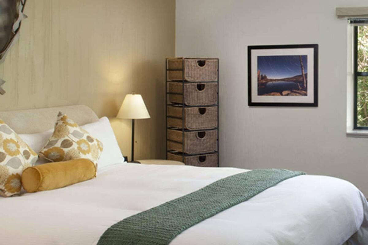 A neatly made bed with a green throw, a ceiling fan, and a framed picture on the wall.