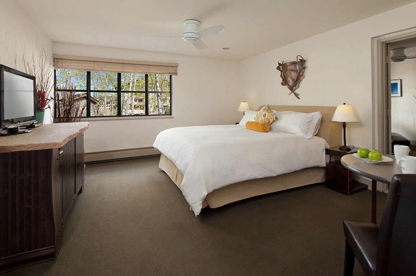 A hotel room with a bed, bedside tables, a TV, a window with a view, and a ceiling fan.