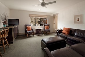 A living room with a sofa, two armchairs, a coffee table, a TV, and a ceiling fan.