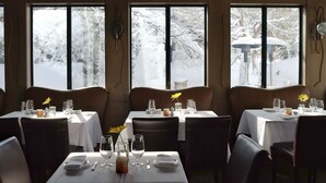 Un restaurante con mesas dispuestas para comer, amplias ventanas con vista nevada y un ambiente cálido.