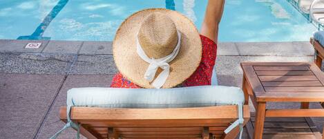 A poolside area with lounge chairs, umbrellas, and a person holding a drink.