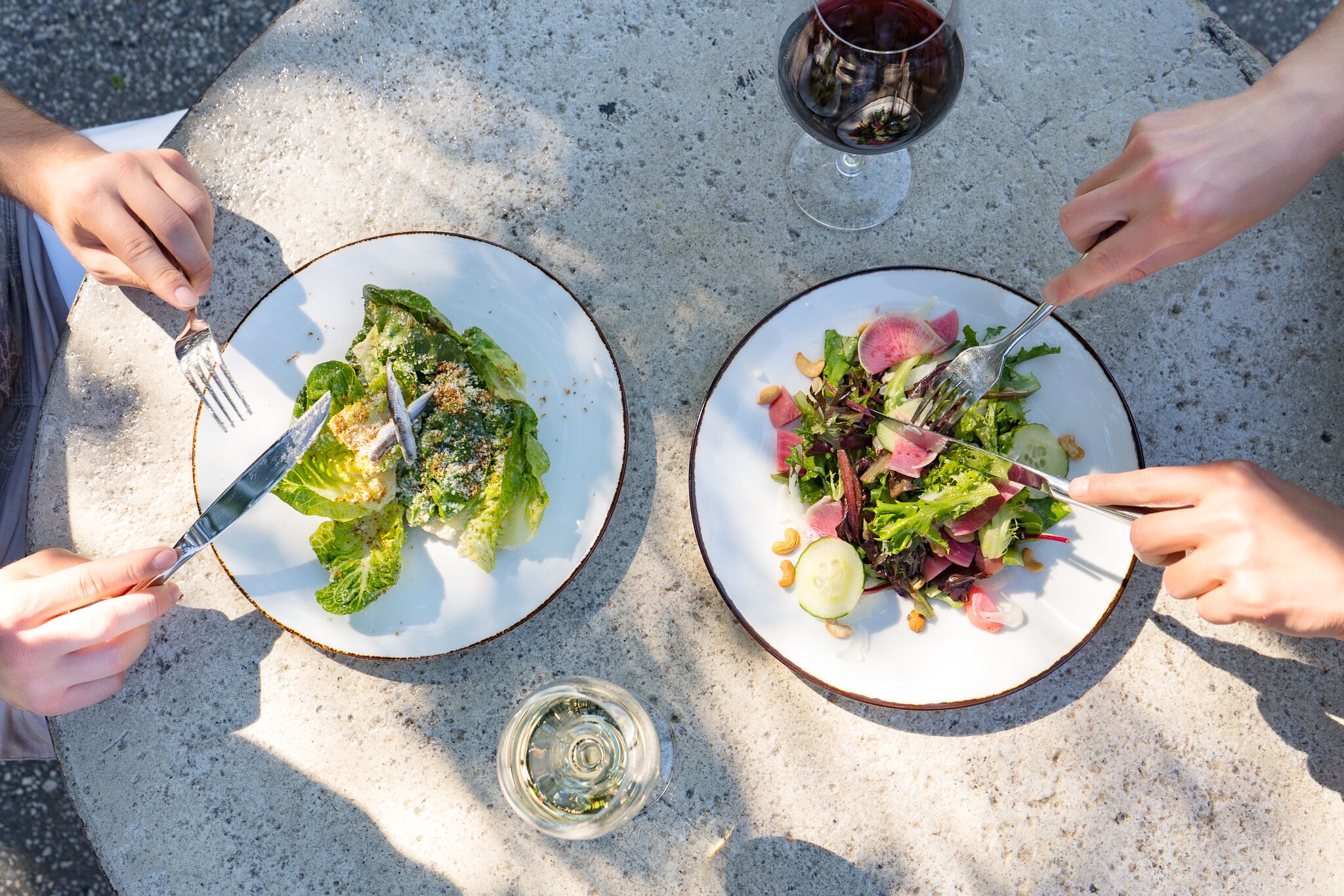 Dos platos de ensalada sobre una mesa con tenedores y una copa de vino.