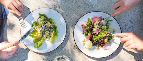 Two plates of salad on a table with forks and a glass of wine.