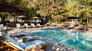 A pool area with lounge chairs and umbrellas, surrounded by trees and a rocky backdrop.