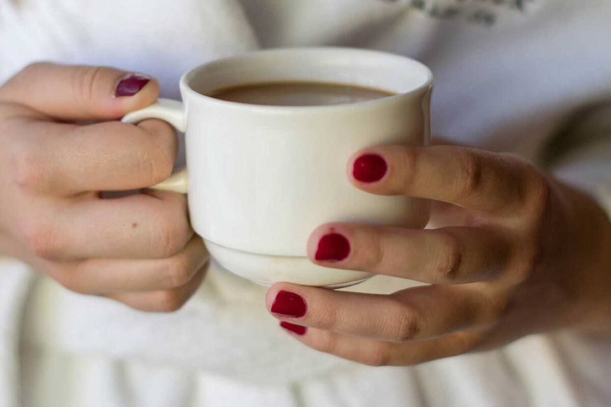 A person holding a white mug with red nail polish.