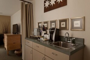 A compact kitchen with a built-in sink, a coffee maker, and framed pictures on the wall.