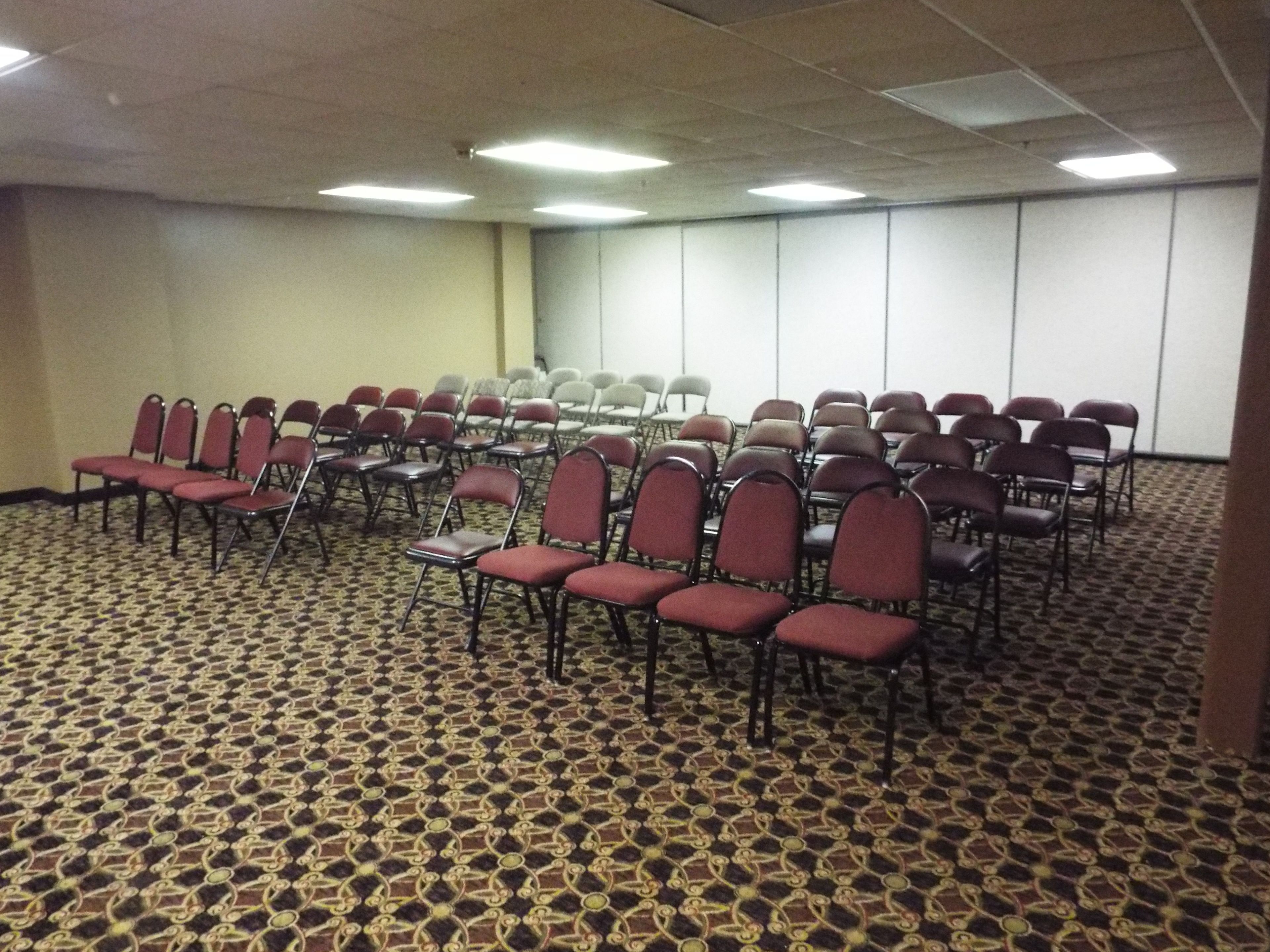 A conference room with rows of chairs and tables, carpeted floor, and ceiling lights.
