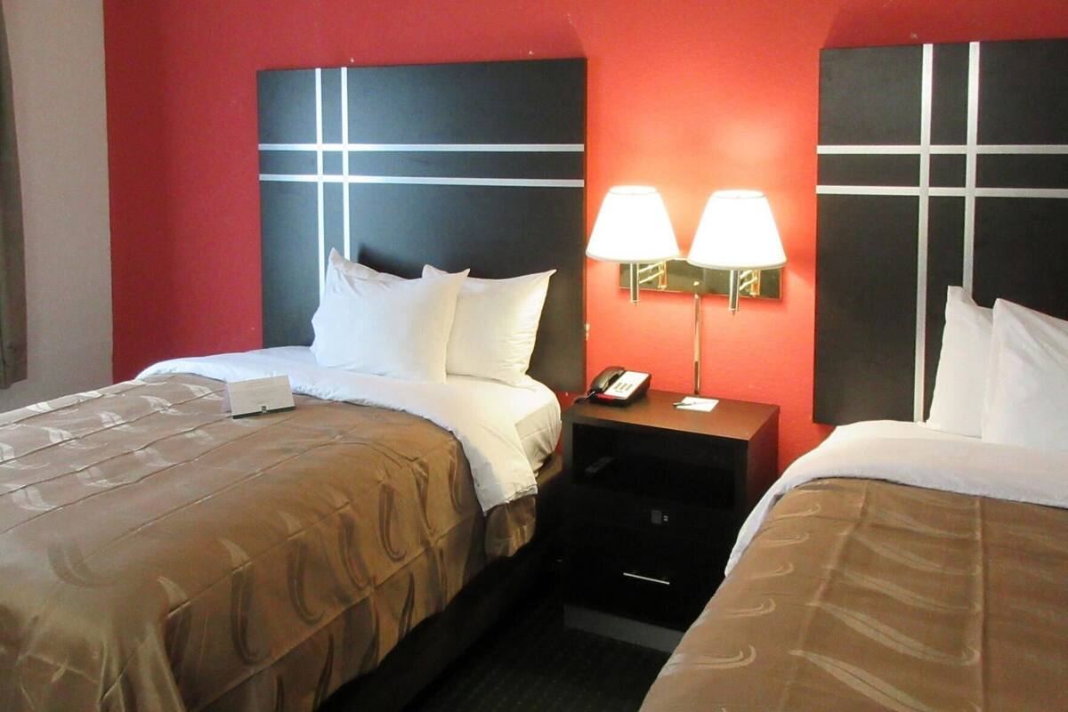 Een hotelkamer met twee bedden, een nachtkastje met een lamp en een telefoon.