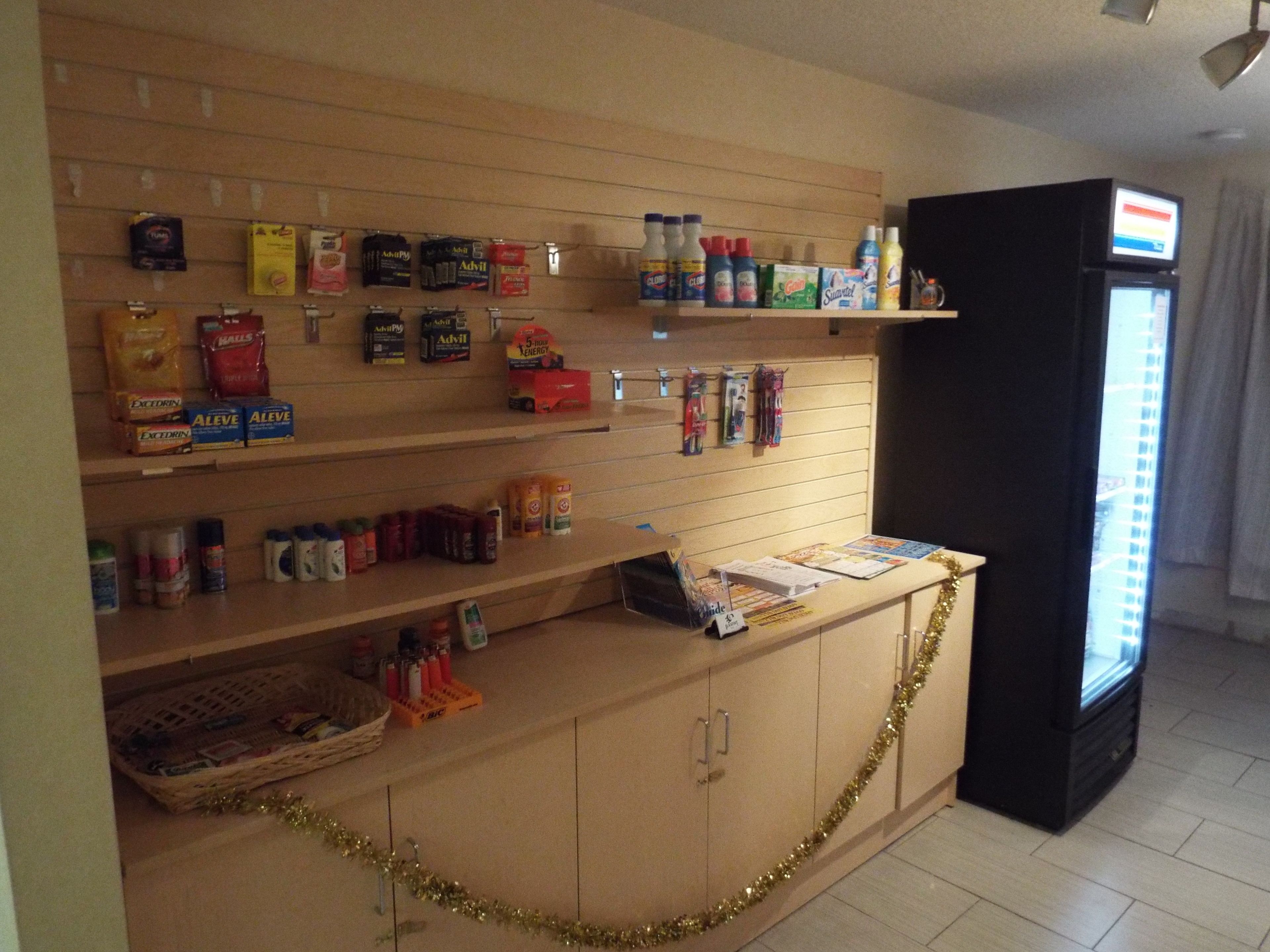 A store with shelves stocked with various products, a counter with promotional materials, and a refrigerator.