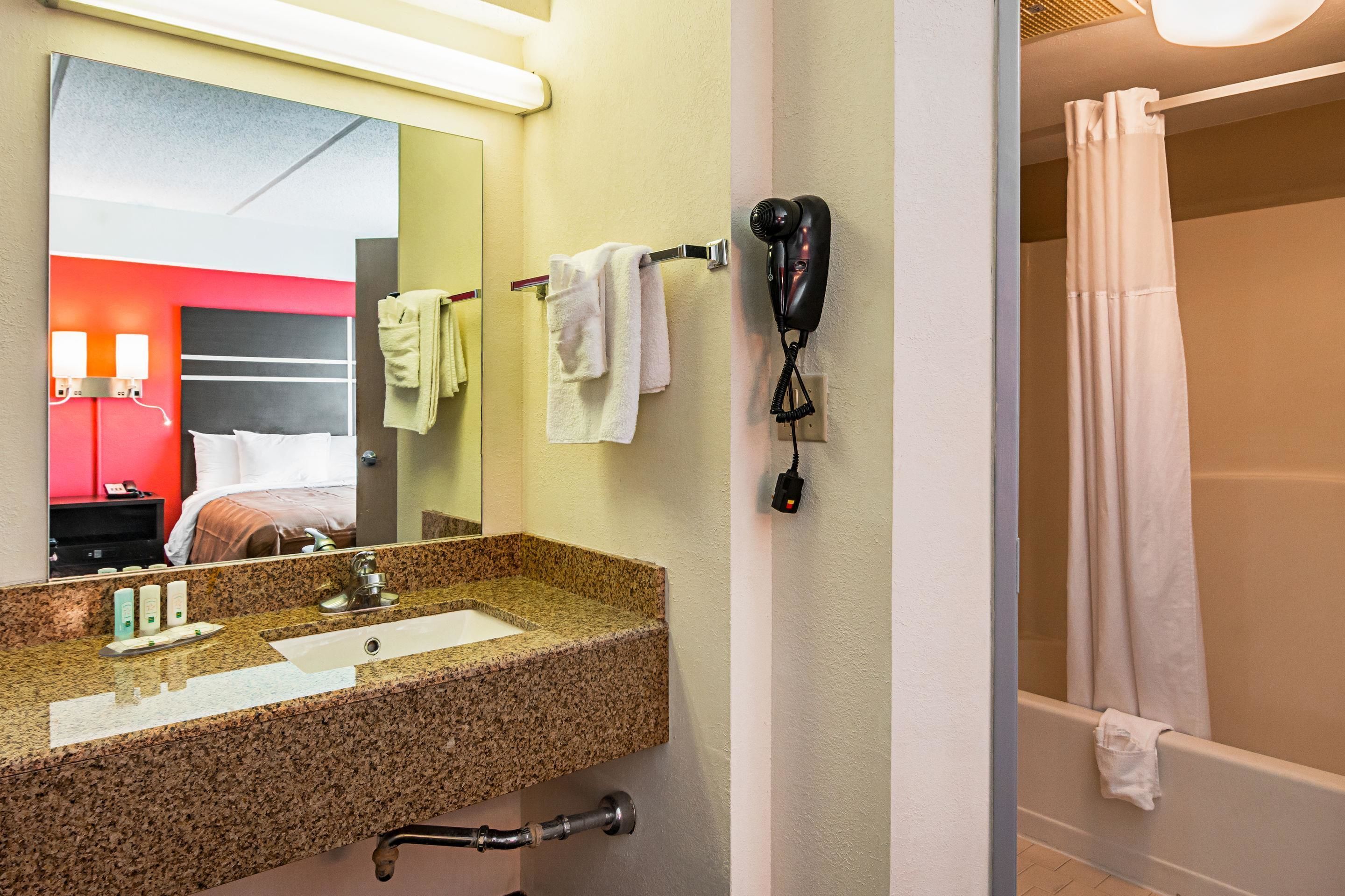 Un baño de hotel con lavamanos de granito, secador de pelo y cortina de ducha.
