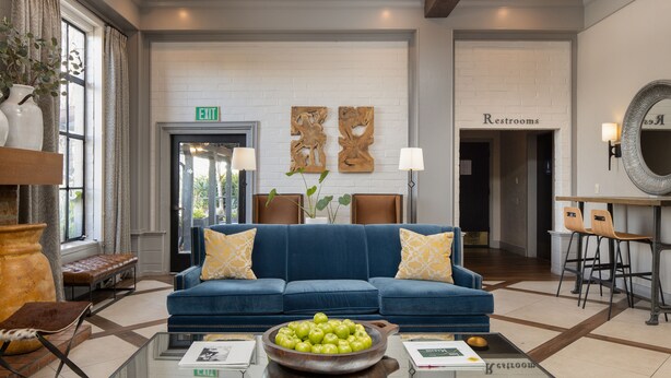 A lobby with a blue sofa, a bowl of apples, a glass coffee table, and a reception desk with a mirror. - Inn Marin and Suites, an Ascend Collection Hotel (Novato)