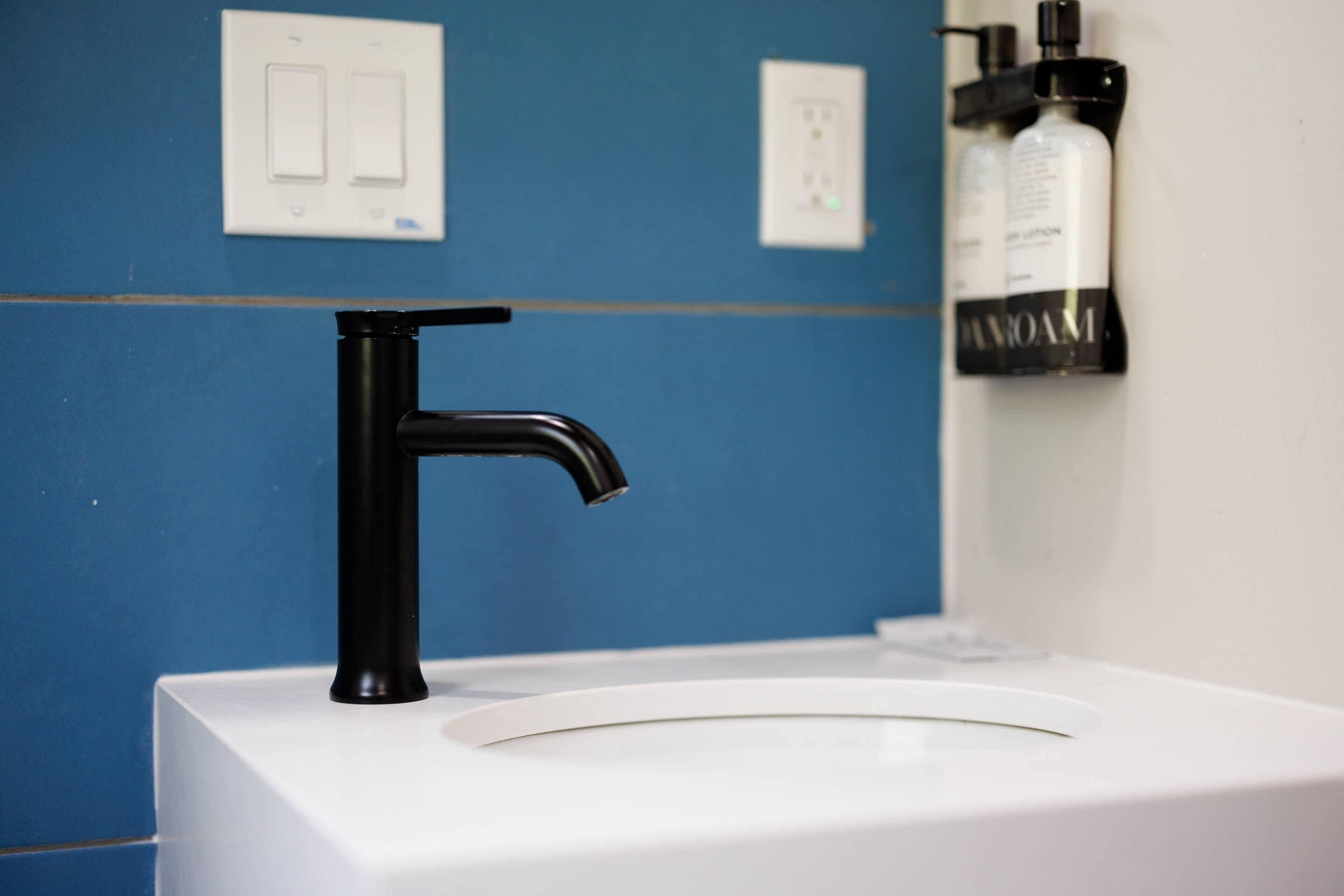 A bathroom with a white sink, a black faucet, and a blue wall.