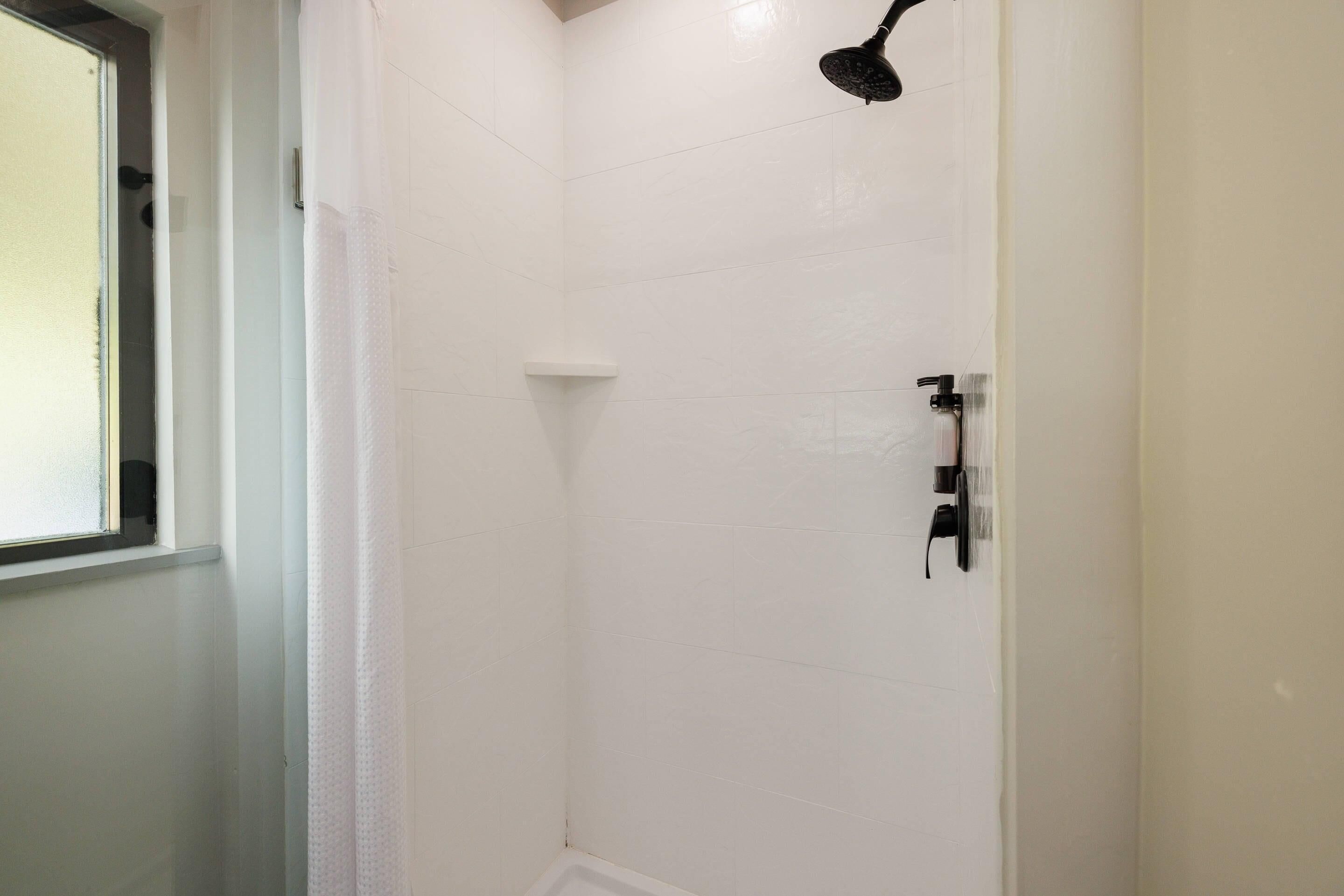 A shower area with white tiles, a showerhead, and a window.