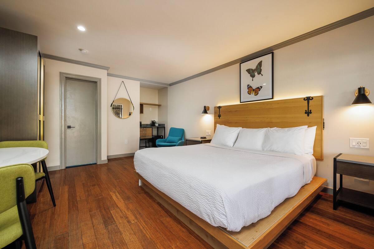 A hotel room with a large bed, a desk, a chair, and a small table.