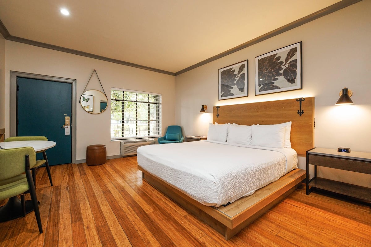 A bedroom with a wooden bed, a desk, a chair, a window with blinds, and two wall-mounted lamps.