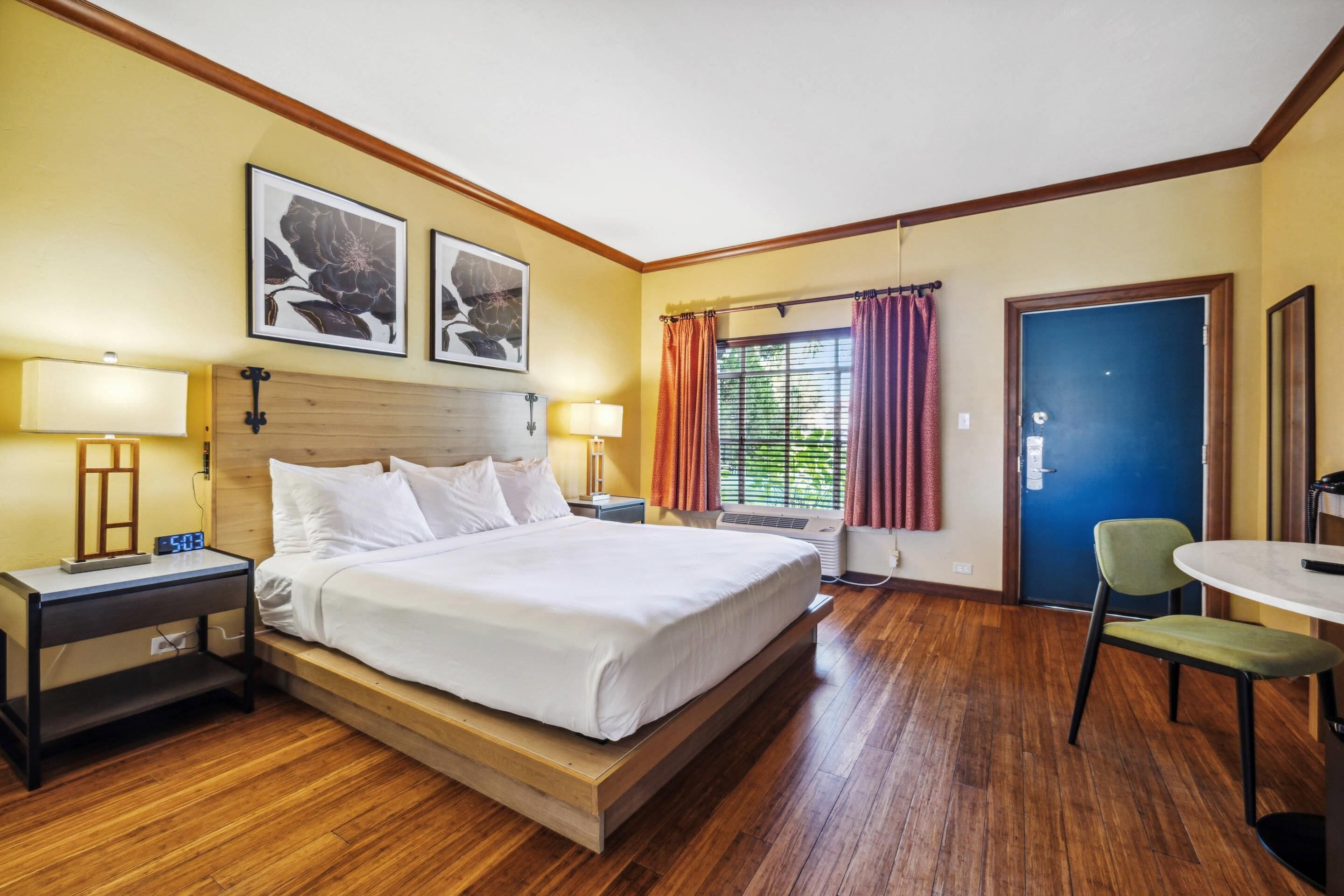 A hotel room with a bed, bedside tables, a desk, a chair, and a window with curtains.