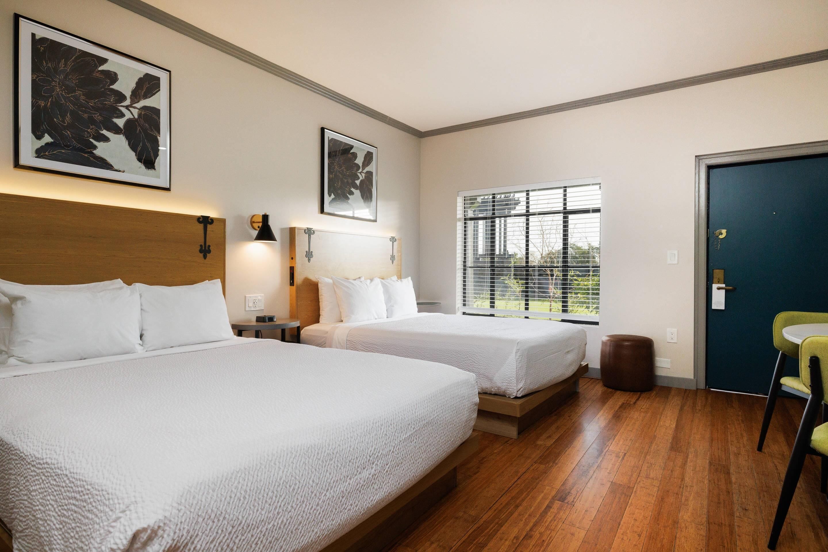 Une chambre d’hôtel avec deux lits, une fenêtre avec des stores, une porte et une chaise.