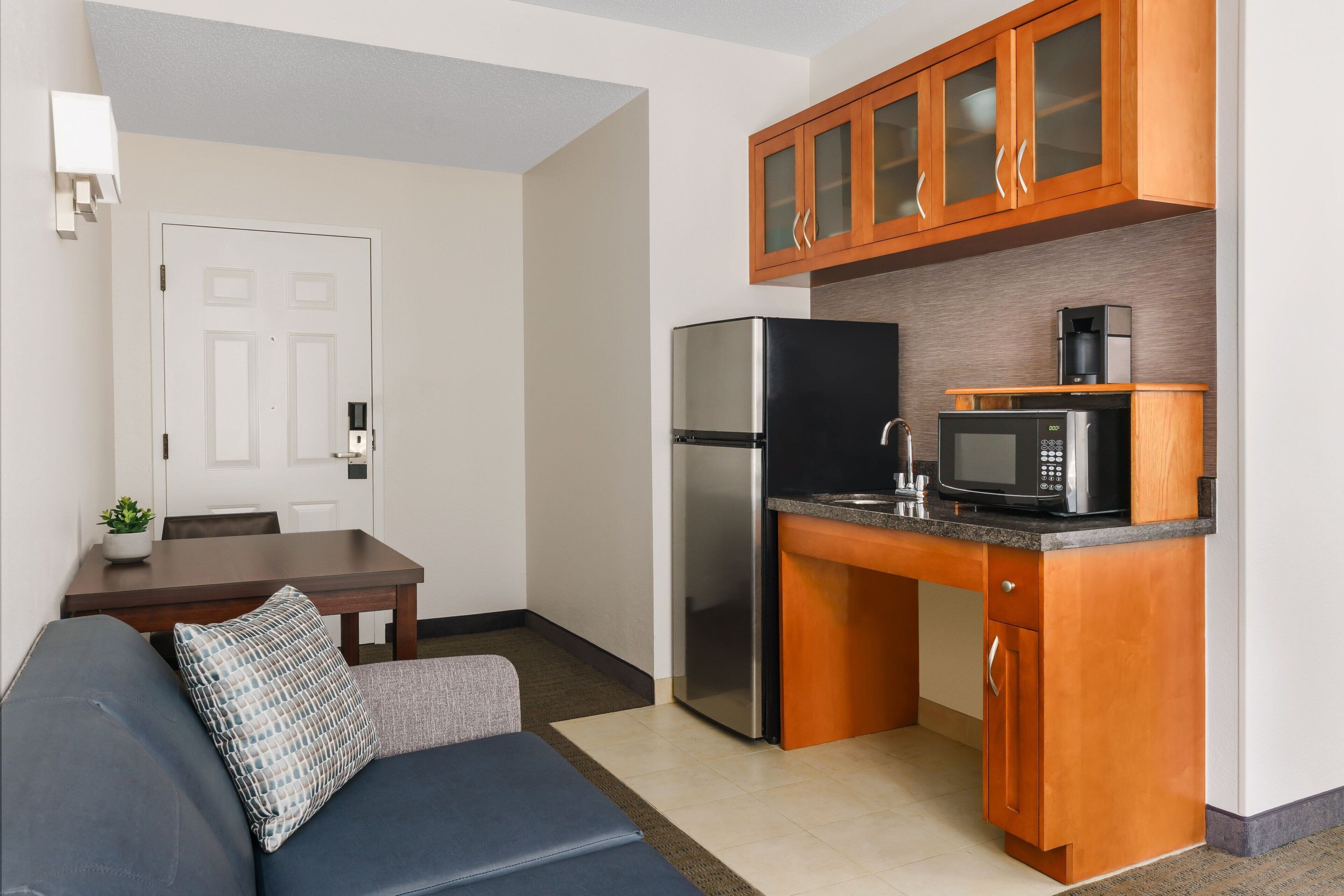 A compact kitchen with wooden cabinets, a stainless steel refrigerator, and a microwave.