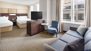 Ein Hotelzimmer mit Bett, Sofa, Fernseher, kleinem Tisch und einem Fenster mit Vorhängen.